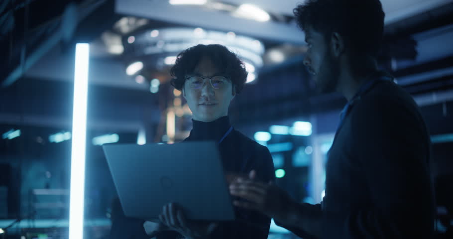 Two Diverse Male Engineers Monitoring Performance of a Quantum Computer. Asian Tech Scientist and Indian Software Developer Having a Conversation and Brainstorming Machine Learning Ideas