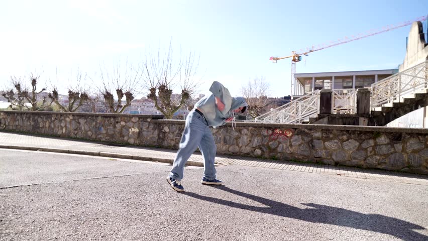 Confident young male dancer performing dynamic freestyle moves on sunny urban street, expressing personal style and passion through energetic movement