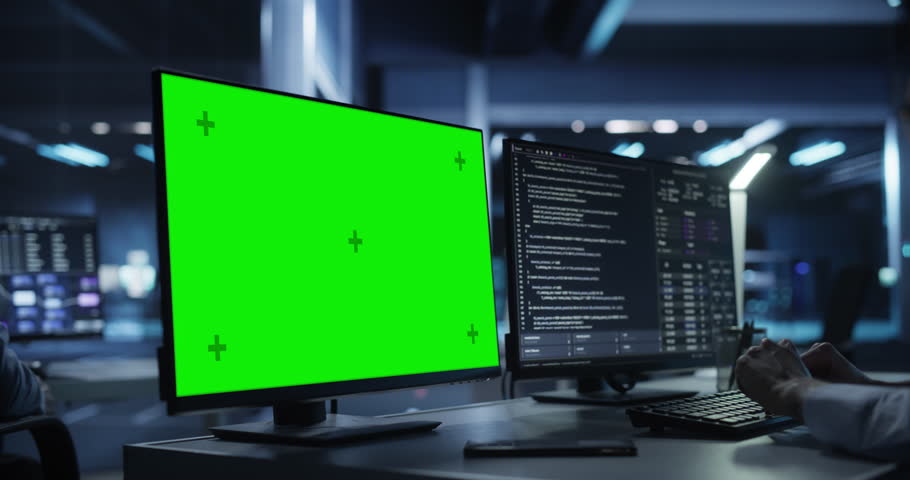 Anonymous Software Developer Working Behind a Desk on a Computer with Green Screen Chromakey Display. Engineer Writing Source Code, Creating Software for a Technological Online Product