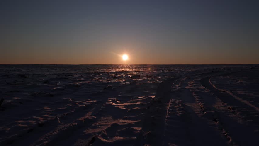 Bright sun on dark blue sky setting over snow field at sunset. Minimalistic winter landscape. Nature background