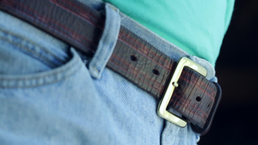 Pulling a brown leather belt tight on a pair of blue denim jeans. Shot with a