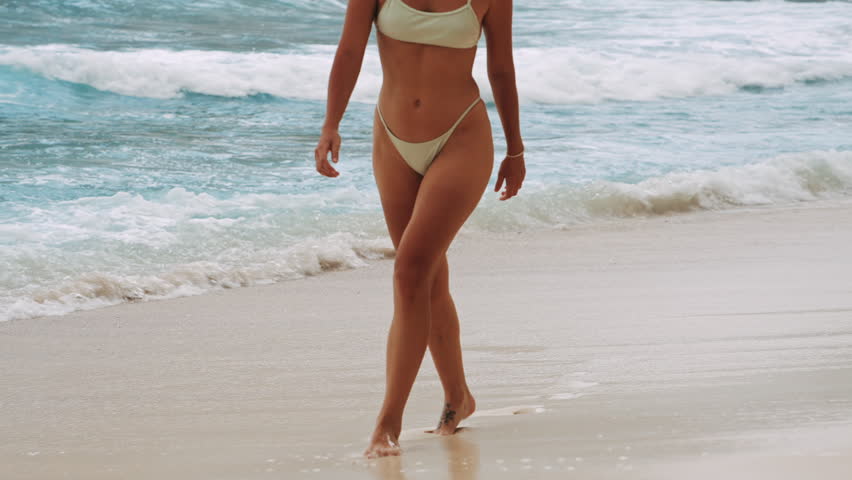 beautiful girl in bikini walking along the beach shoreline