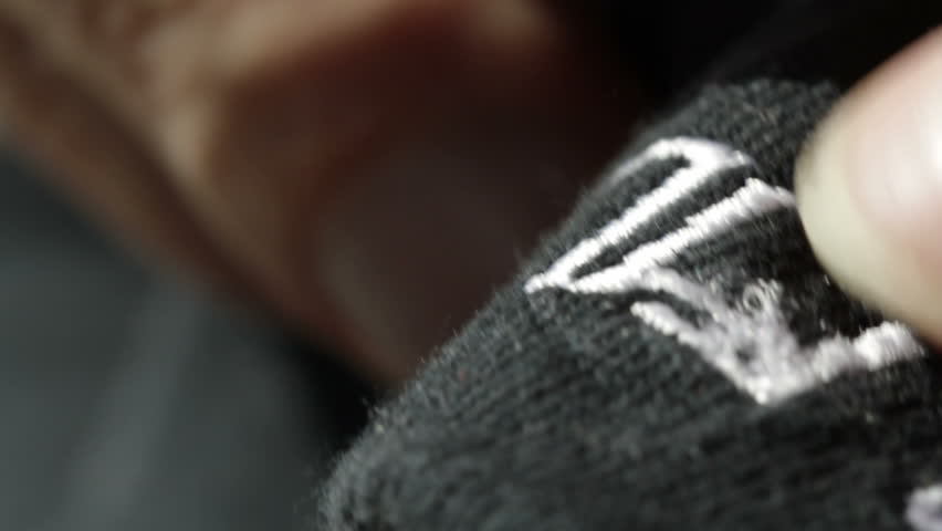 Unpicking the stitches from an embroidered design on black material. Shot with