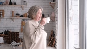 Beautiful middle aged woman drinking tea near window in the kitchen - Powered by Shutterstock - Get 15% off with code: PIKWIZARD15