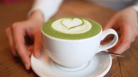 Delicate female hands carefully serving aromatic matcha latte featuring elegant heart-shaped design atop polished wooden surface inside warm, inviting cafe environment - Powered by Shutterstock - Get 15% off with code: PIKWIZARD15