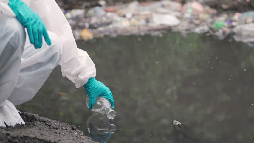 Scientist in Protective Gear Collecting Water Sample from Polluted River for Environmental Analysis, ecology concept