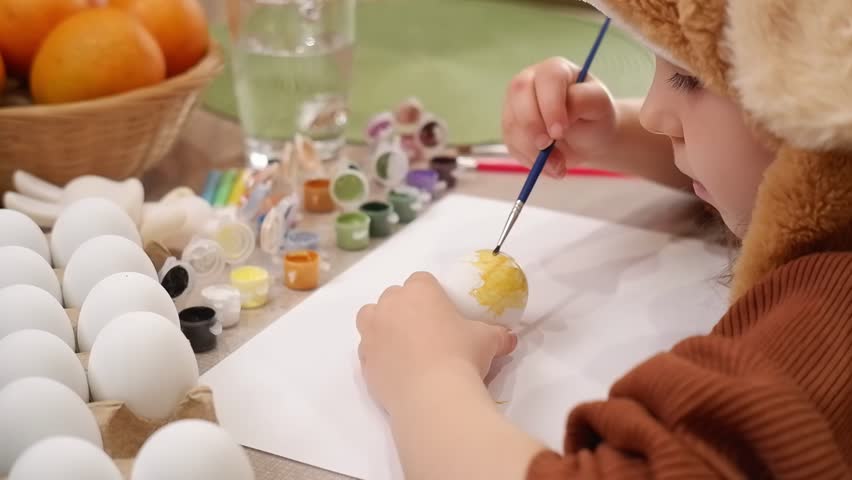 Young artist carefully painting easter eggs with yellow tempera color