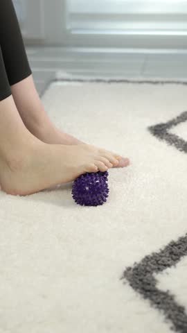 Vertical video, Woman is training with foot massage ball from muscle pain and stress. Relaxation massage after hard work day. 4k footage.