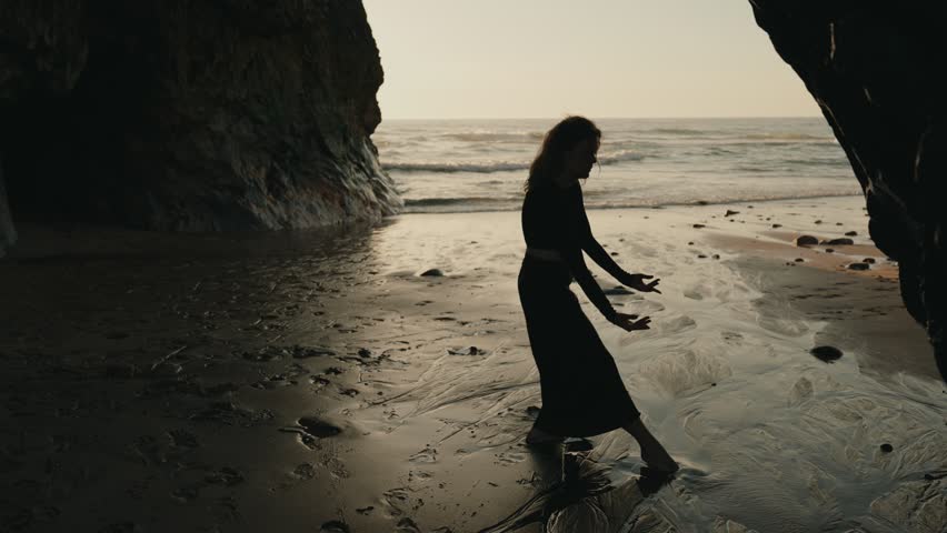 A graceful female dancer performs a silhouette dance on a serene beach at sunset, embodying freedom and elegance by the ocean shore.
