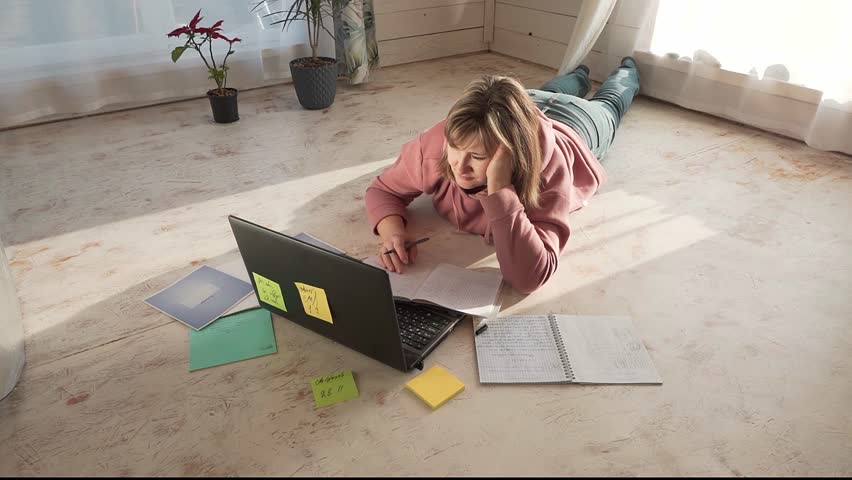 Woman lying on the floor and working on a laptop. Remote work concept.