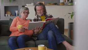 Elderly couple sharing tender moments on comfortable sofa, browsing through cherished photo album while sipping warm beverages and reminiscing about precious memories - Powered by Shutterstock - Get 15% off with code: PIKWIZARD15