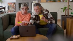 Happy retired couple using laptop and credit card, enjoying online shopping together on comfortable sofa in cozy living room, having coffee and snacks - Powered by Shutterstock - Get 15% off with code: PIKWIZARD15