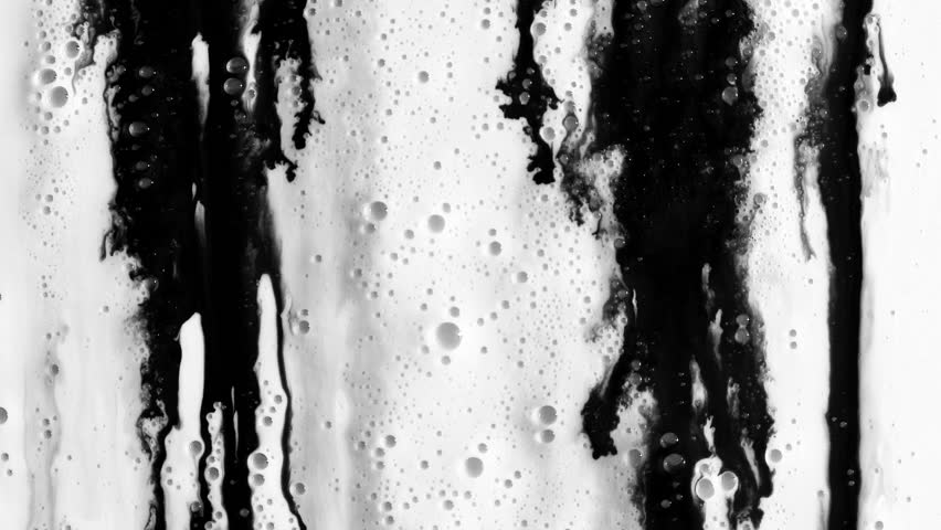 Black liquid flowing and spreading across a foamy white liquid surface.