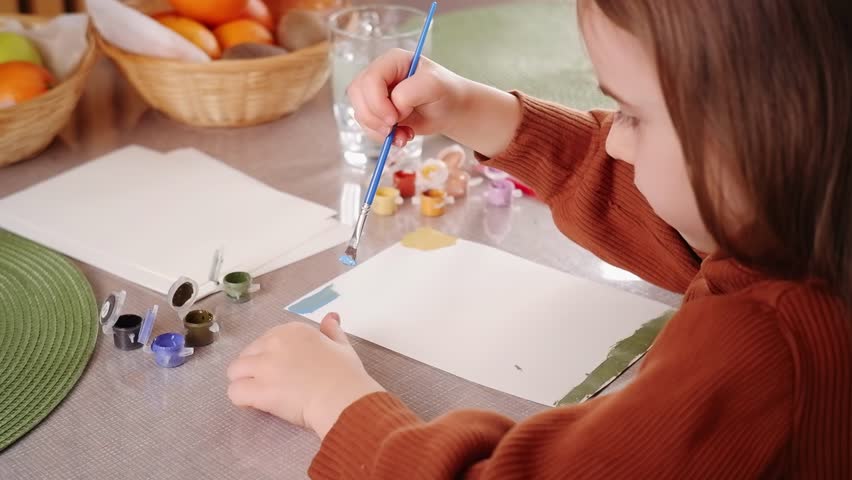 Young girl painting on a white sheet of paper with tempera colors