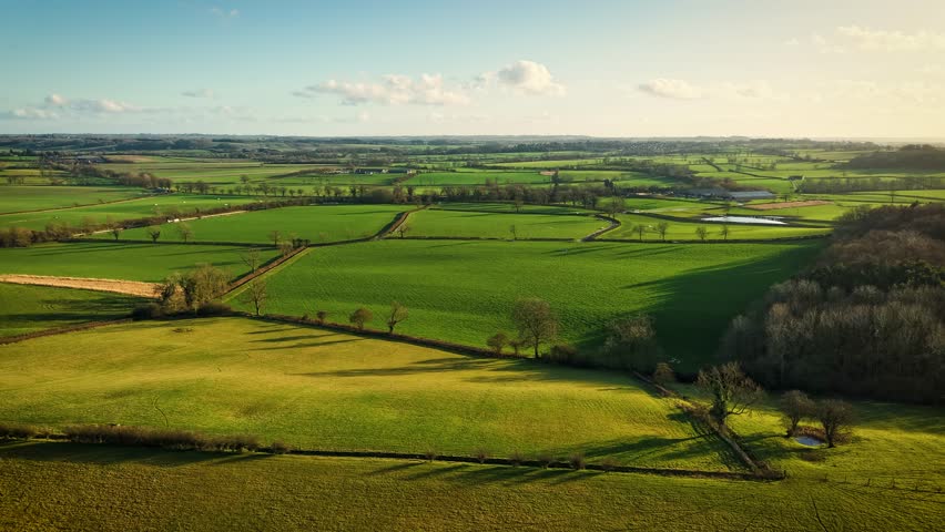 Timelapse Green fields in countryside with moving clouds under golden sunlight. Endless Rolling meadows in farming land hyperlapse. Vast rural landscapes with pastures and shimmering daylight