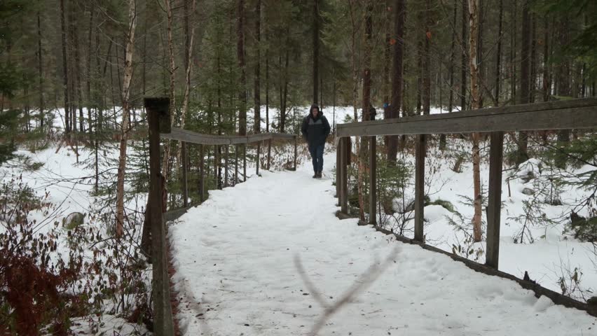 A Caucasian man with hoodie and backpack hiking in the snow-covered Algonquin