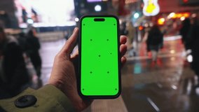 Pov look at male hand holding smartphone keylight green screen gadget in street at night, man walking crowded crosswalk, camera locked on phone chroma key display, bokeh evening city background - Powered by Shutterstock - Get 15% off with code: PIKWIZARD15