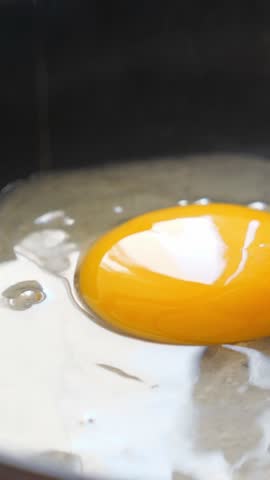 Pouring egg on frying pan. Cooking fried eggs, closeup. Vertical footage