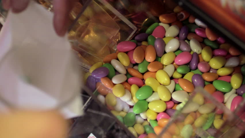 Sugared almonds being scooped from a selection in a candy store and into a paper