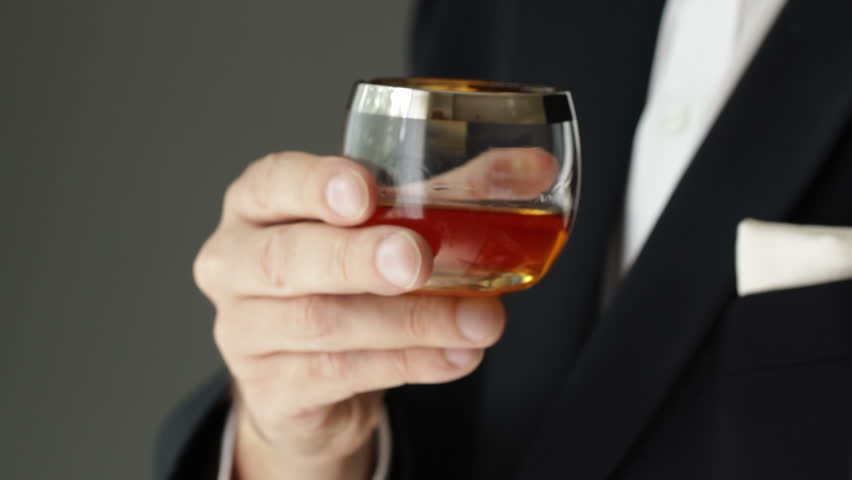 Whisky drinker wearing a tuxedo presents a glass of whisky to the camera.