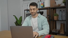 Young man celebrating success at work with clenched fists while using laptop in a modern office setting, surrounded by plants and shelves. - Powered by Shutterstock - Get 15% off with code: PIKWIZARD15