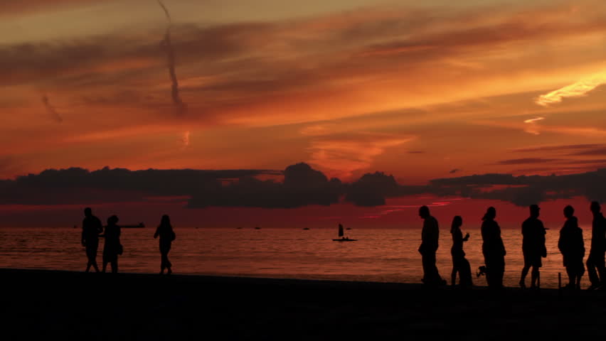 Groups of people silhouetted against a sunset sky as they walking on the