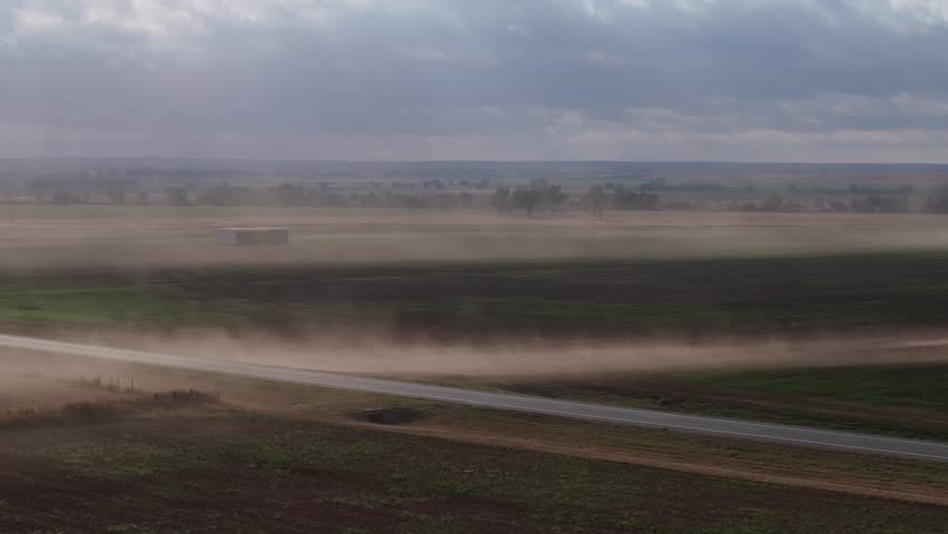 Dusty wind sweeping across Oklahoma highway with distant barns and farmland visible