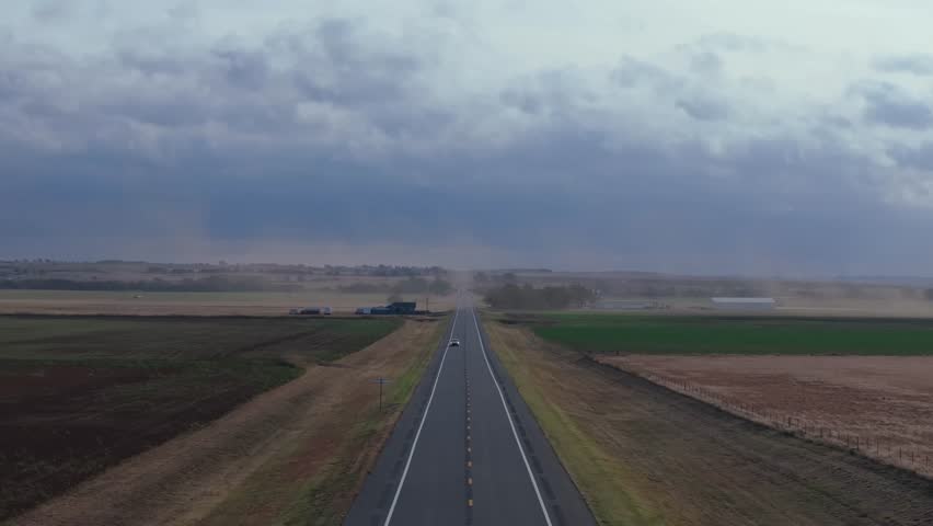 Wide, empty highway in Oklahoma with strong winds kicking up dust across fields