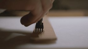 A craftsman presses a pronged leather chisel into a strip of leather, creating evenly spaced holes for stitching in a detailed close-up view. - Powered by Shutterstock - Get 15% off with code: PIKWIZARD15