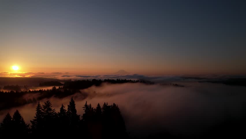 Aerial: foggy fire sky sunrise over Mount Rainier (Tahoma) with clouds and skyscape in Cascade Range, Mount Rainier National Park, west-central Washington state, USA, pan drone shot