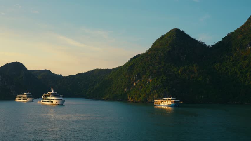 Cruise ships in Morning Sunlight at Halong Bay during sunrise with Green Karst Mountains in Backdrop, Vietnam - aerial