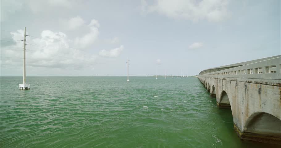 Wide static shot of bridge in the Florida Keys with power lines on the left. Some traffic seen driving. For projects requiring longer clips in higher resolution, visit StockPlates.