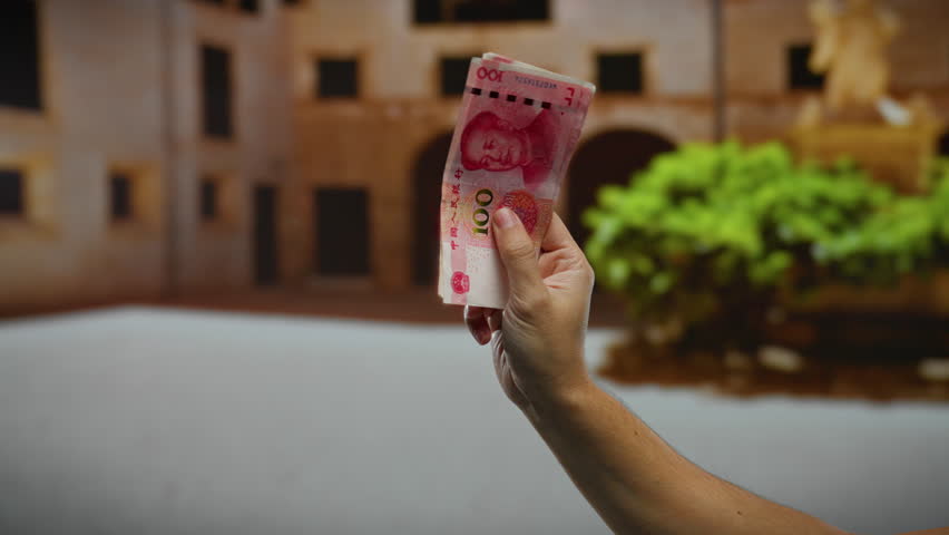 Man holding chinese yuan banknotes on a city street, showcasing business and currency exchange outdoors with a blurred urban background.