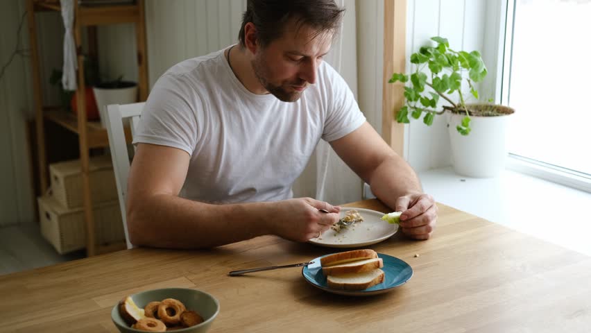 Handsome bearded man is eating green fresh vegan salad in the kitchen at home. Male sitting at table and eats vegetables, lettuce vegetarian meal. Happy athlete male enjoying Tasty healthy diet food.