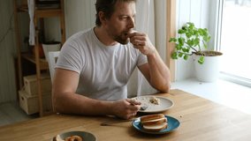 Handsome bearded man is eating green fresh vegan salad in the kitchen at home. Male sitting at table and eats vegetables, lettuce vegetarian meal. Happy athlete male enjoying Tasty healthy diet food. - Powered by Shutterstock - Get 15% off with code: PIKWIZARD15