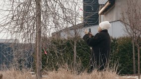 Senior woman pruning tree branches in a winter garden. She wears a thick coat and a knitted hat, carefully trimming the bare branches with pruning shears. High quality 4k footage - Powered by Shutterstock - Get 15% off with code: PIKWIZARD15