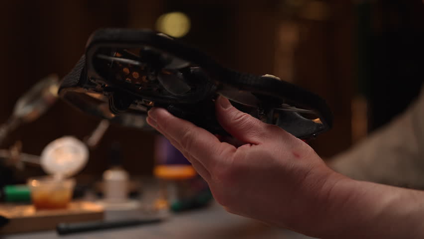 Close-up side view of technician holding and examining small fpv drone in dark workshop, checking propellers and frame among various tools and components. Concept of maintenance and repair process. - Powered by Shutterstock - Get 15% off with code: PIKWIZARD15