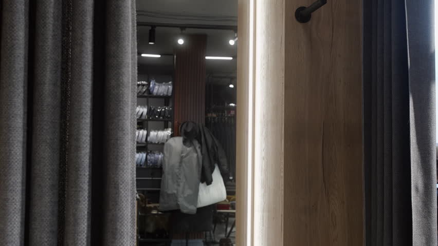Elegant businessman adjusting his suit jacket while looking in the mirror in the dressing room of a menswear store, choosing his outfit for a special occasion or business meeting