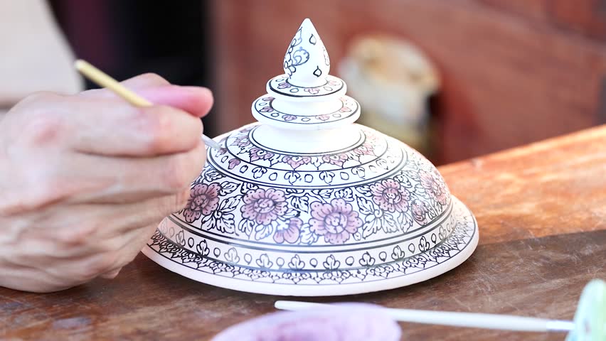 Artist carefully painting intricate patterns on traditional Thai ceramic bowl