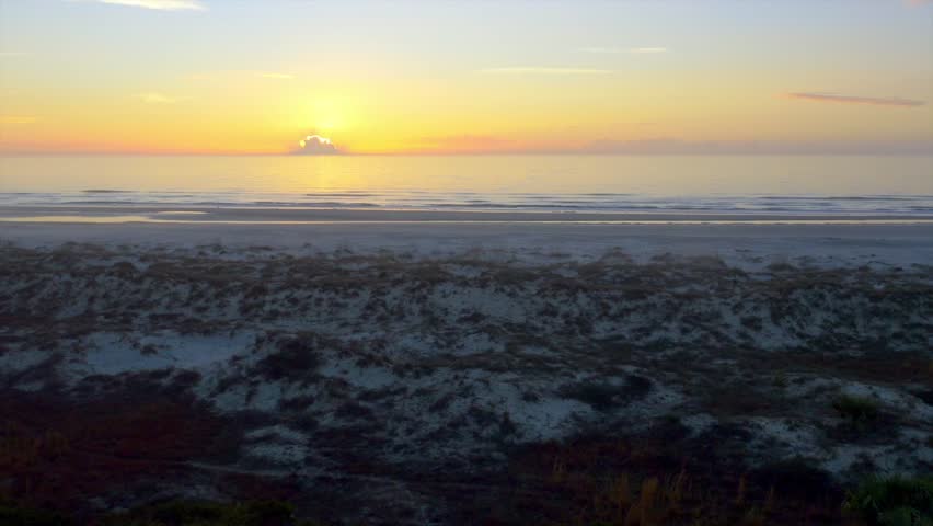 Sandy Beach with Gentle Waves and a Sunset Behind the Clouds