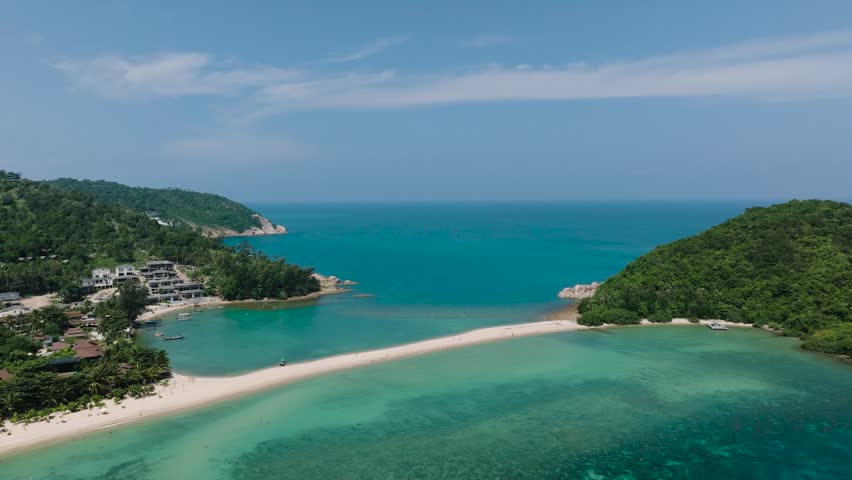 Turquoise sea with a sandy strip between two green hills under a clear blue sky. Ko Ma Beach. Ko Pha Ngan, Thailand.