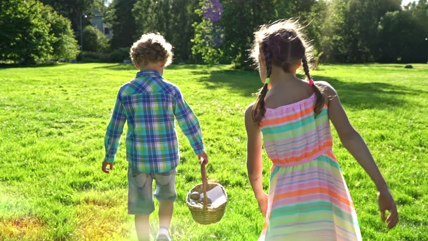 Children joyfully participate in an Easter egg hunt in a sunny park. They gather colorful eggs into a wicker basket and walk barefoot on lush grass, enjoying a cheerful spring celebration.
