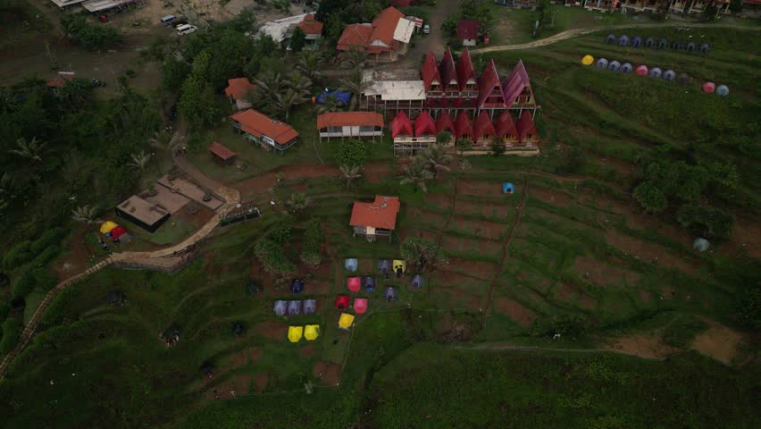 A drone pullback view of tents in a campsite on Menganti Beach Hill overlooking the expanse of the Indian Ocean in Kebumen, Java, Indonesia