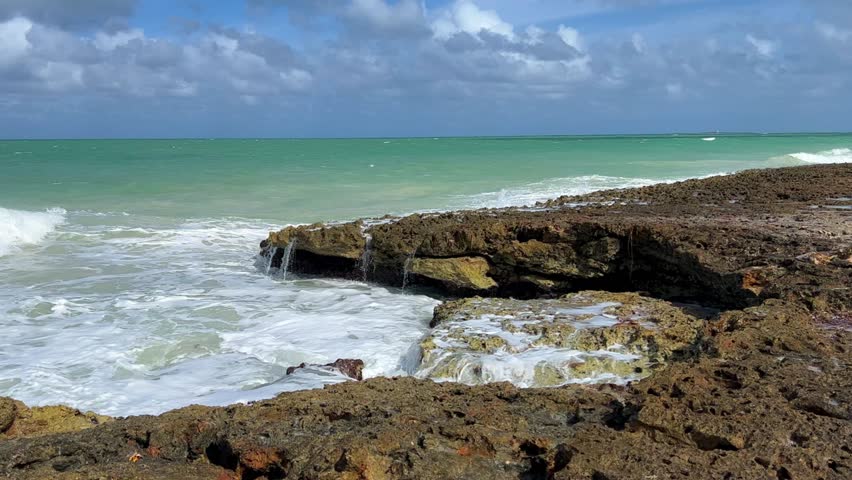 Rocky Cuban beach in Varadero, Cuba, on a cloudy day, when the sun breaks through the clouds, you can see the waves and ocean expanses. Turquoise waves. Stone slabs on the beach in the ocean. 4K	