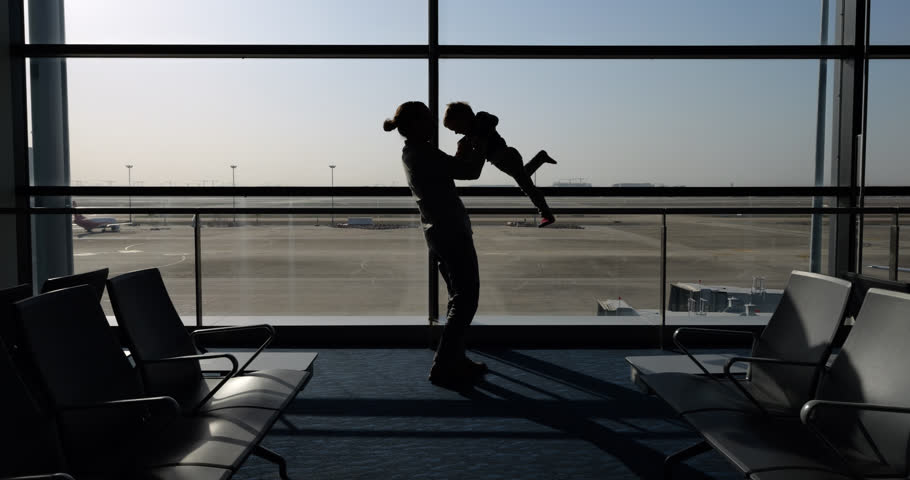 Silhouette of father playing with his little boy in airport terminal, he raise kid up and spinning him around, creating a playful and heartwarming scene. Full length silhouetted shot against window