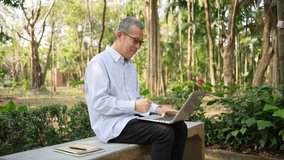Elderly Asian man Sitting on Bench in Park Using Laptop with Joyful Expression Surrounded by Nature Outdoors - Powered by Shutterstock - Get 15% off with code: PIKWIZARD15