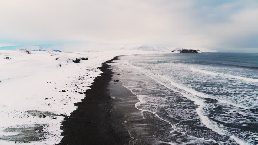 Aerial overview of Iceland frozen beach with dark waves crashing onto the icy shoreline
