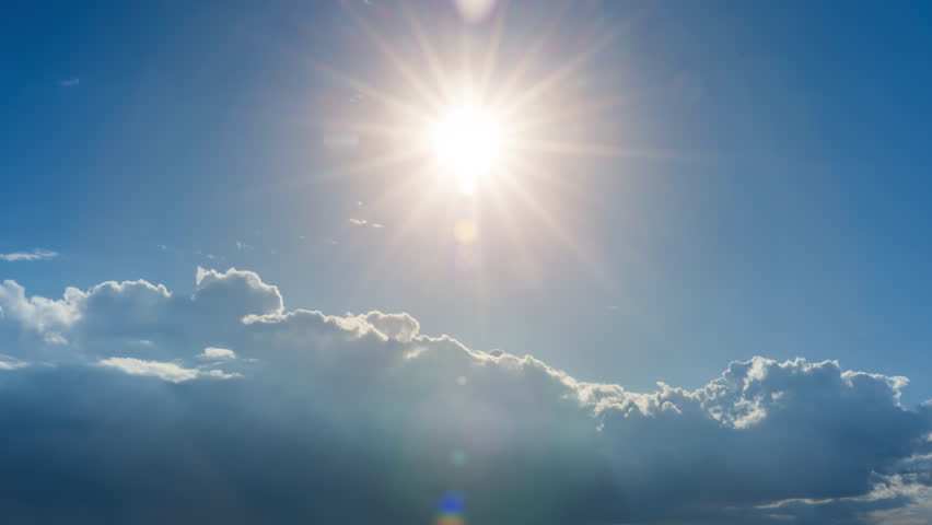 A bright sun shines in a clear blue sky with scattered clouds