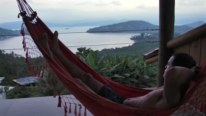 Man Relaxing On Hammock At Villa With Scenic Nature View At Sunset In Brazil. wide static shot