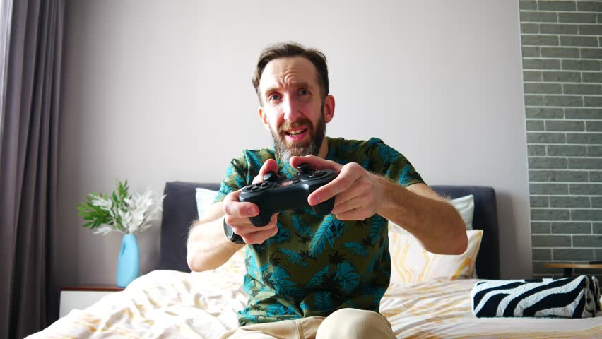 A man plays a video game while sitting on the bed but ends up losing